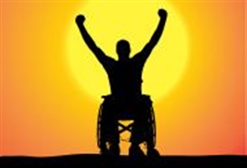 man in wheelchair with arms up in front of sunset